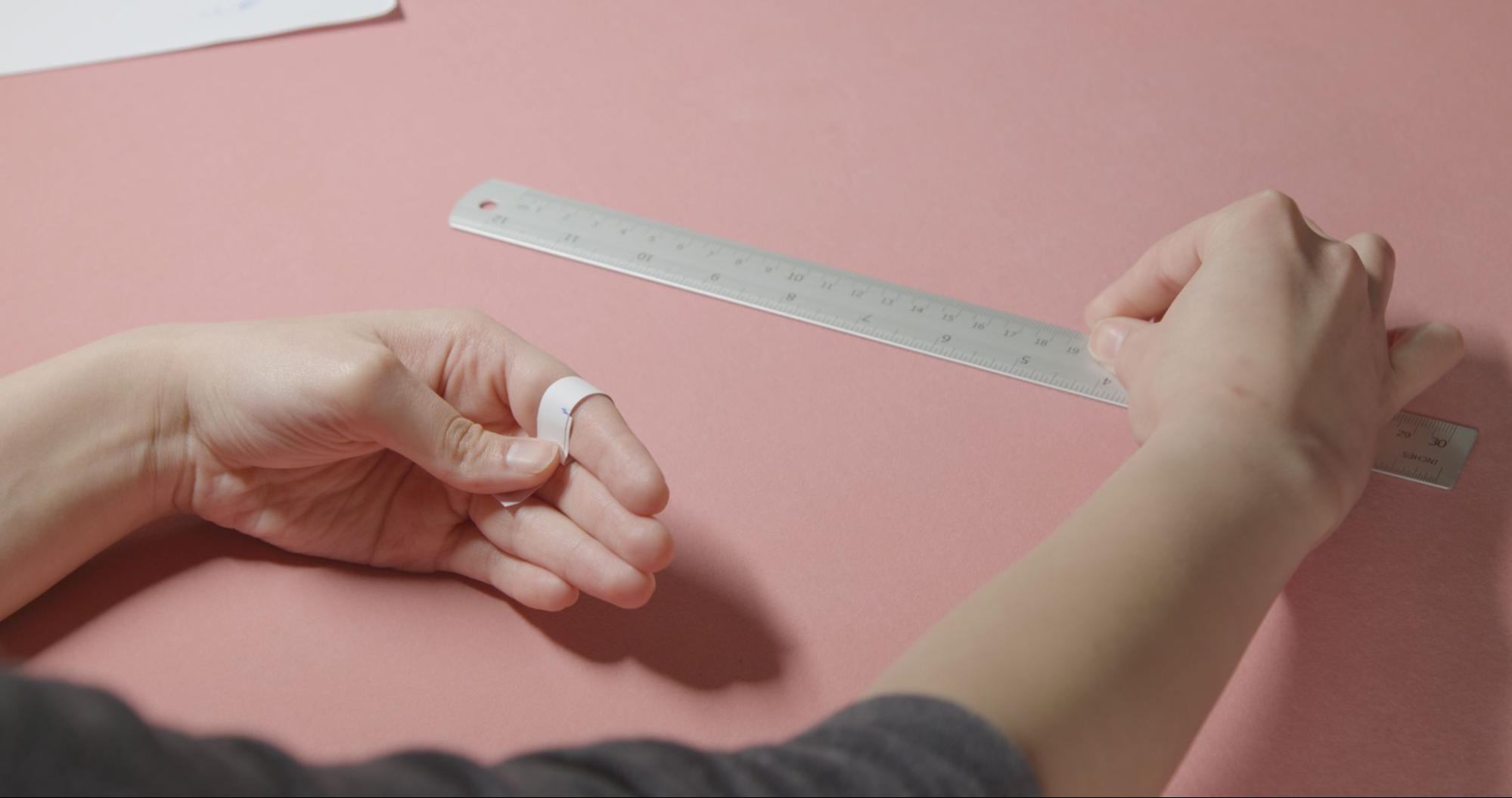 A woman demonstrates how to find a woman's engagement ring with a ruler and measuring band