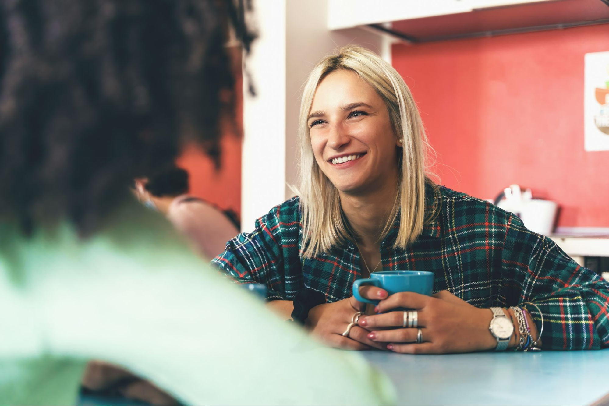 A picture of a smiling woman holding a coffee cup with silver stacking rings on her hands