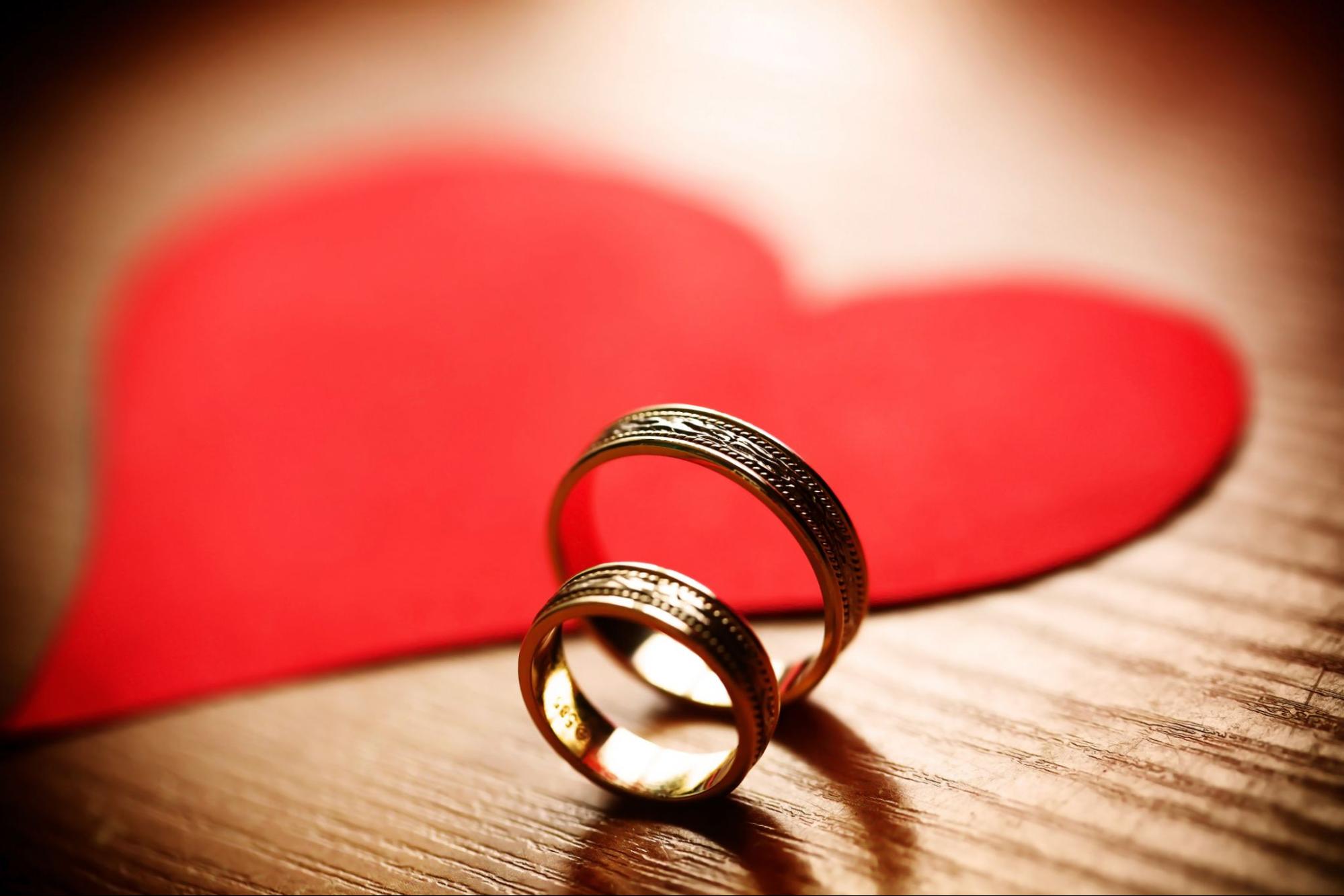 Two rustic vintage wedding bands sit on a dark wood table with a red heart in the background