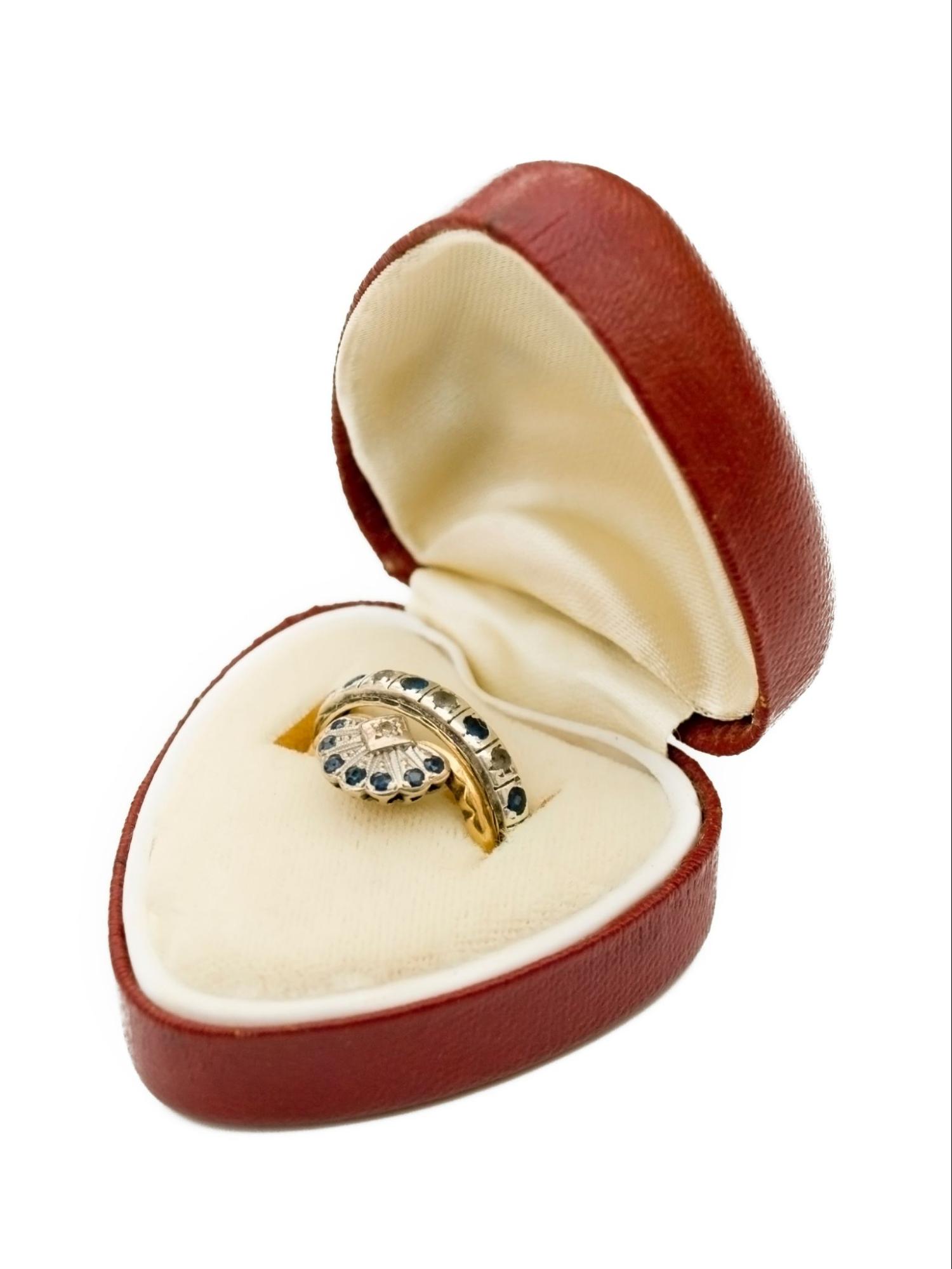 A ring box is open with a sapphire-studded vintage wedding band inside