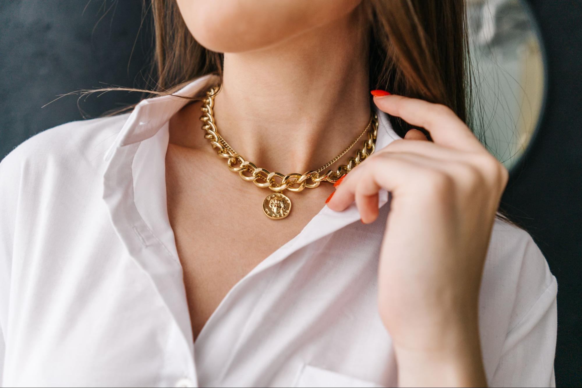 A close up of a woman in a white button up wearing a yellow gold chunky chain necklace