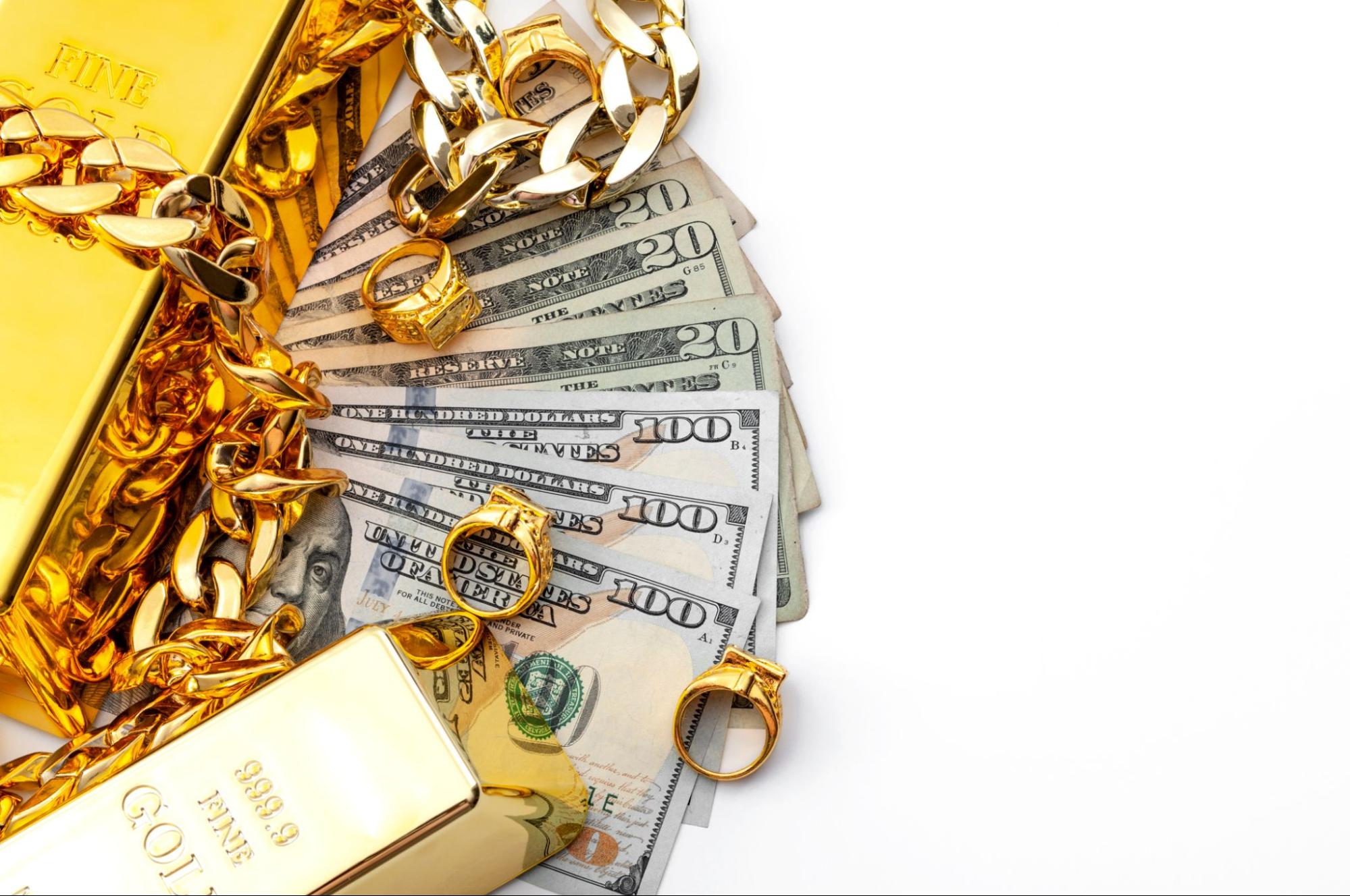 Gold rings, gold chains and two gold bars sit atop a pile of cash 