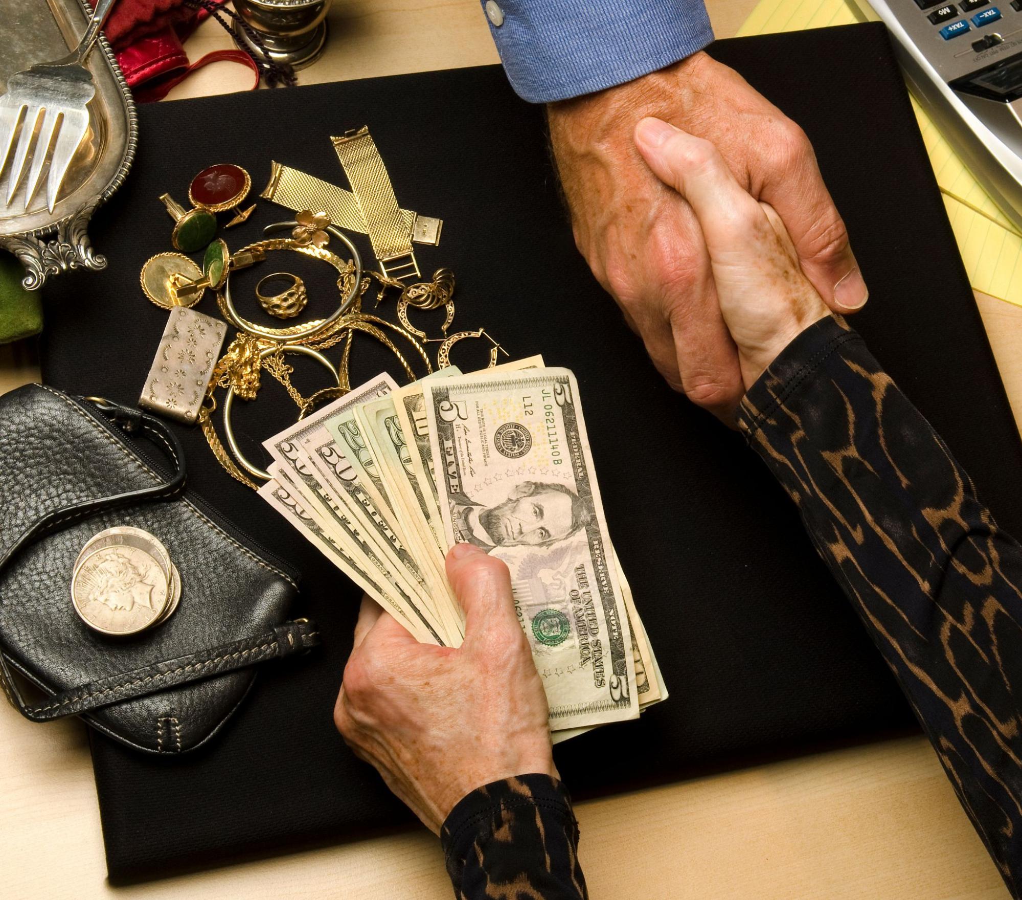 A woman shakes hands with a jewelry buyer and accepts cash in exchange for her gold jewelry